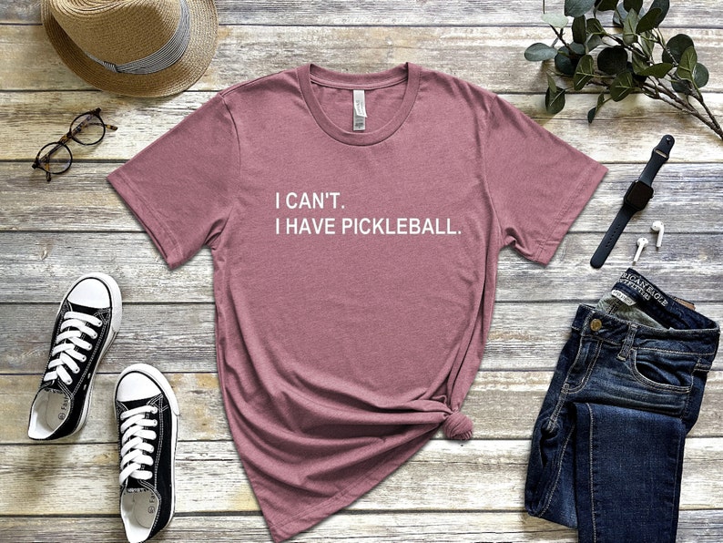 May include: A mauve t-shirt with the text "I CAN'T. I HAVE PICKLEBALL." printed in white.