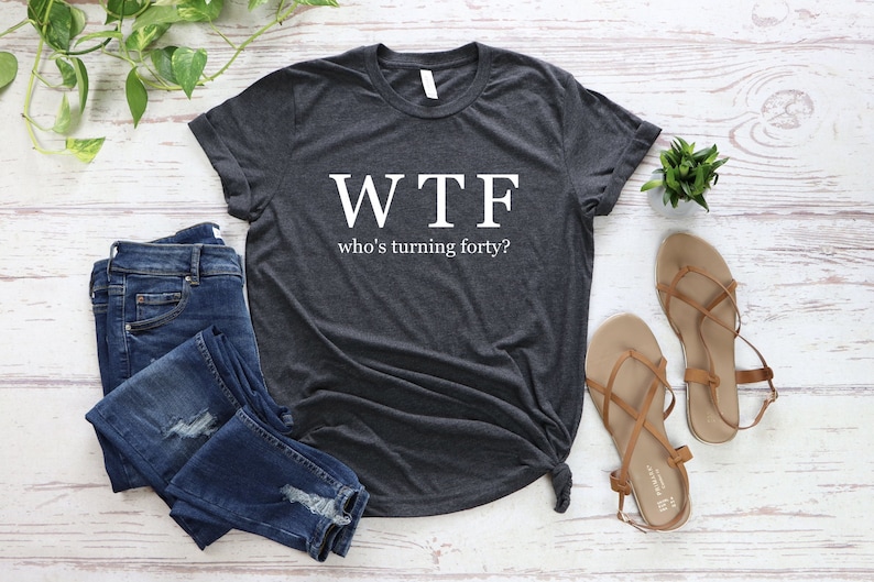 K&ouml;nnte beinhalten: Ein dunkelgraues T-Shirt mit dem Aufdruck "WTF who's turning forty?" in wei&szlig;.