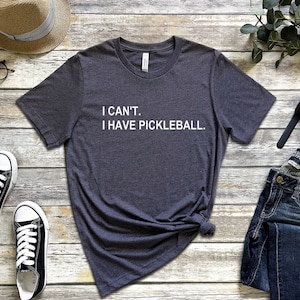 May include: A dark gray t-shirt with the text "I CAN'T. I HAVE PICKLEBALL." printed in white.