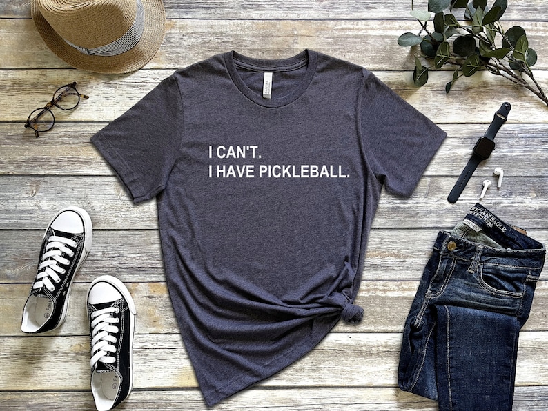 May include: A dark gray t-shirt with the text "I CAN'T. I HAVE PICKLEBALL." printed in white.