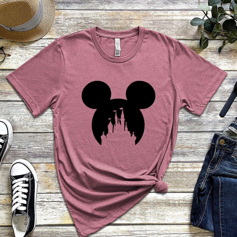 May include: A pink t-shirt with a black silhouette of Mickey Mouse's head with the silhouette of Cinderella's castle inside the ears.