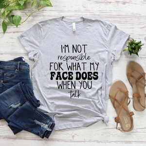 May include: A heather grey t-shirt with the text "I'm not responsible for what my face does when you talk" printed in black.