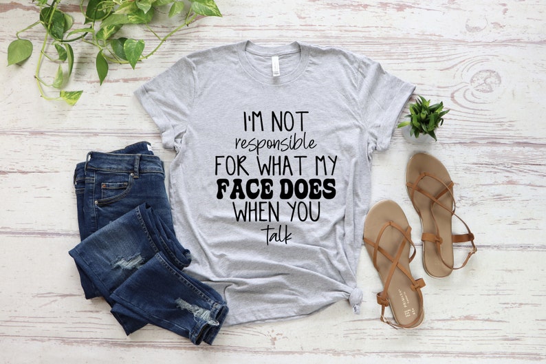 May include: A heather grey t-shirt with the text "I'm not responsible for what my face does when you talk" printed in black.