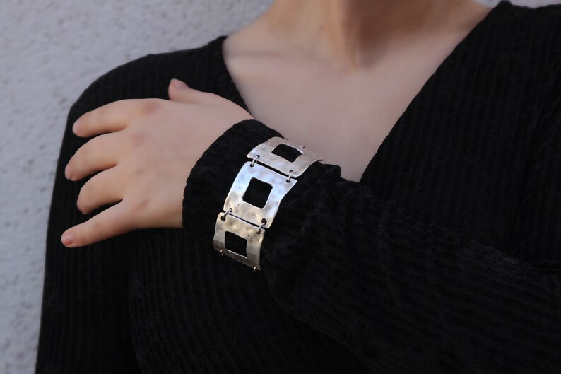 May include: A silver bracelet with a geometric design. The bracelet is made of multiple connected squares with cutouts.