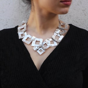 May include: A silver necklace with a geometric design. The necklace is made of multiple interconnected square shapes, creating a modern and edgy look.