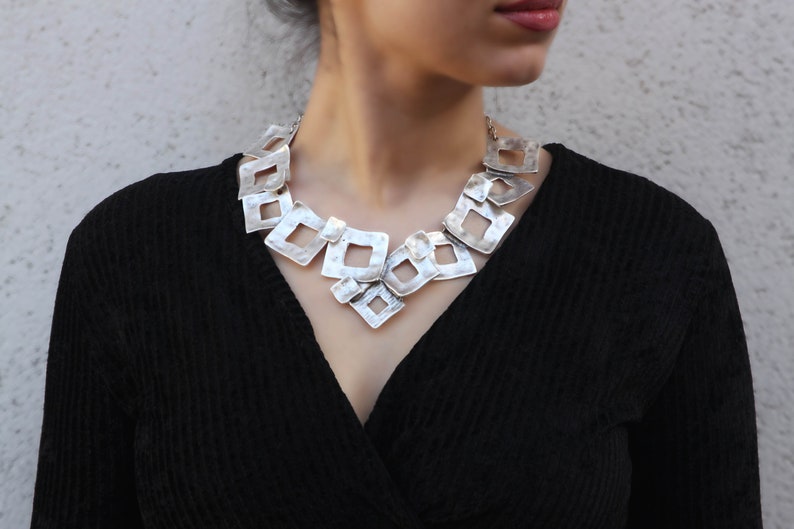 May include: A silver necklace with a geometric design. The necklace is made of multiple interconnected square shapes, creating a modern and edgy look.