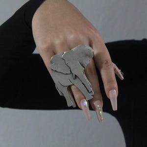 Puede incluir: Un anillo de plata con un dise&ntilde;o de elefante detallado. El anillo se lleva en el dedo &iacute;ndice de una mano con u&ntilde;as largas de color rosa claro.