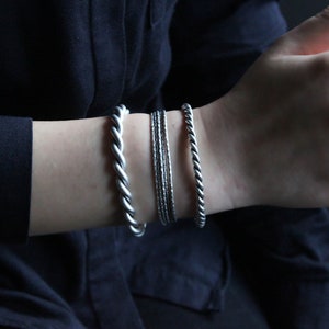 Puede incluir: Una muñeca con cuatro pulseras de plata. Las pulseras son de diferentes estilos, pero todas están hechas de metal trenzado.