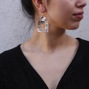 May include: Silver earrings with a hammered square design. The square has a smaller square cut out in the center.