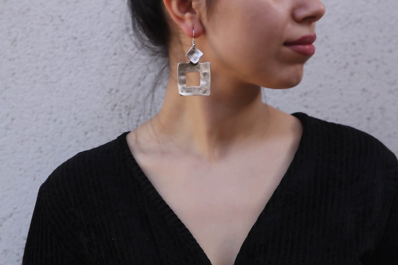 May include: Silver earrings with a hammered square design. The square has a smaller square cut out in the center.