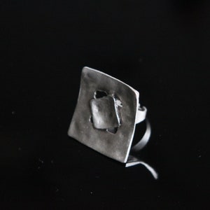 May include: A silver ring with a square-shaped design featuring a cut-out geometric pattern.