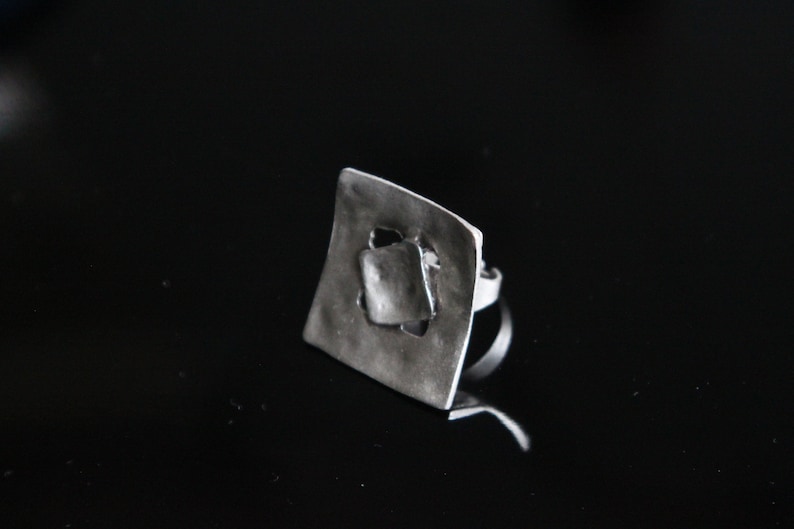 May include: A silver ring with a square-shaped design featuring a cut-out geometric pattern.
