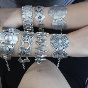 Può includere: Un set di braccialetti d'argento con disegni intricati. I braccialetti presentano vari motivi, tra cui cerchi, fiori e forme geometriche.