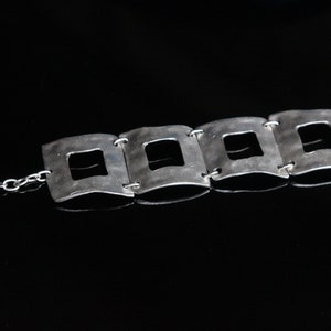 May include: A silver bracelet with a chain and four square links, each with a square cutout in the center.