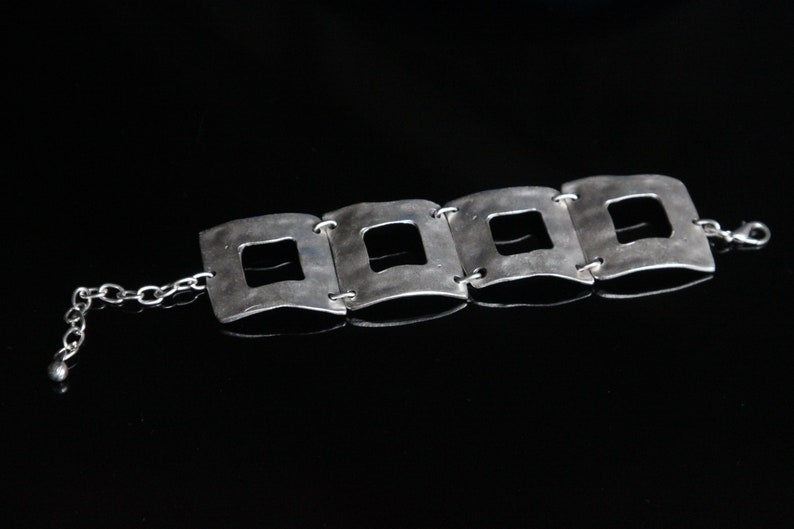 May include: A silver bracelet with a chain and four square links, each with a square cutout in the center.