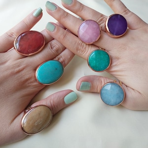 May include: Six oval and round gemstone rings with rose gold settings. The rings feature a variety of colors, including pink, purple, turquoise, green, brown, and blue.