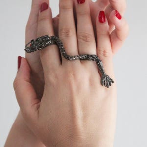 May include: A silver dragon ring with a detailed design. The ring is worn on the middle finger of a hand with red nail polish.