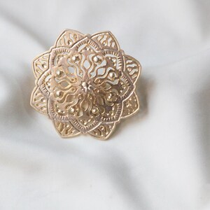 May include: A gold-coloured metal ring with a detailed mandala design.