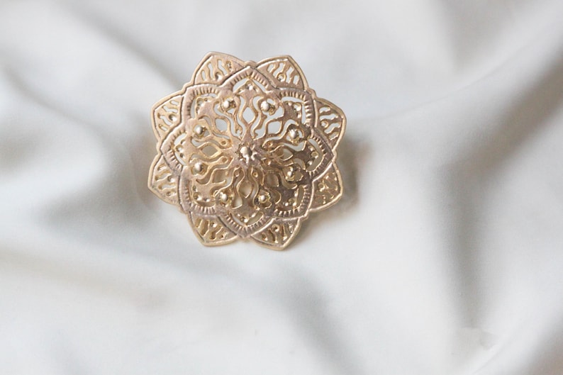 May include: A gold-coloured metal ring with a detailed mandala design.
