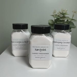 May include: Three clear plastic jars with black lids filled with white powder. The labels read "Abercrombie & Fitch", "Narcissist", and "Mahogany Coconut" carpet freshener. The jars are on a white surface.