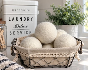 May include: A rectangular wire basket with a beige fabric liner and lace trim, filled with several off-white felted wool dryer balls. The basket features dark metal wire construction and is positioned near a white laundry bin with black text.
