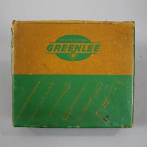 Op de afbeelding: Een bruine kartonnen doos met een groen label waarop "Tools for Craftsmen GREENLEE" en een groen-wit logo staan. De doos heeft een groene achtergrond met illustraties van schroevendraaiers.