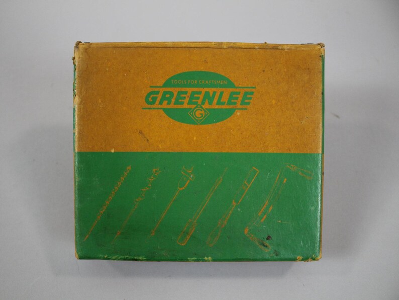 Op de afbeelding: Een bruine kartonnen doos met een groen label waarop "Tools for Craftsmen GREENLEE" en een groen-wit logo staan. De doos heeft een groene achtergrond met illustraties van schroevendraaiers.
