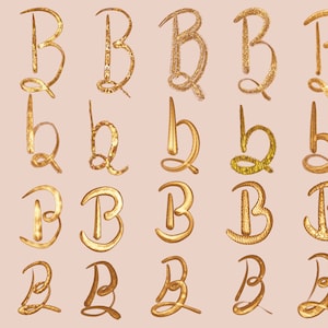 May include: A set of 20 gold glitter letter Bs in various styles. The letters are arranged in five rows of four letters each. The letters are all in a cursive style and have a glittery finish.