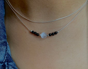 May include: A silver chain necklace with a white gemstone bead and black beads. The necklace is layered with two chains.