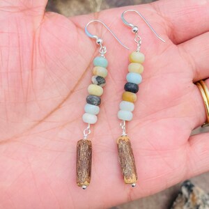 Peut inclure: Boucles d'oreilles faites &agrave; la main avec un m&eacute;lange de perles rondes color&eacute;es dans les tons de bleu, jaune et gris, enfil&eacute;es sur du fil d'argent. Les boucles d'oreilles sont finies avec une petite perle en bois cylindrique en bas.