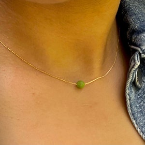 May include: A delicate gold chain necklace with a single round green stone pendant.