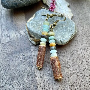 Peut inclure: Boucles d'oreilles artisanales compos&eacute;es de perles color&eacute;es et de pendentifs cylindriques en bois. Les perles sont de diff&eacute;rentes couleurs : bleu, vert, marron et jaune. Les crochets d'oreilles sont de couleur dor&eacute;e. Bijou unique.
