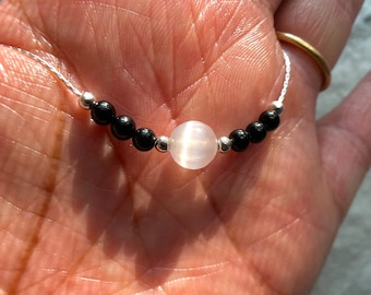 May include: A silver chain necklace with black and white beads. The center bead is a large, white, round gemstone.