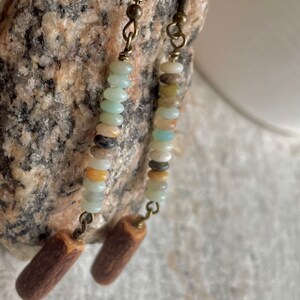 Peut inclure: Boucles d'oreilles faites &agrave; la main avec une cascade de petites perles color&eacute;es dans les tons de bleu, beige et marron. Les perles sont enfil&eacute;es sur un fil et fix&eacute;es &agrave; un charm en bois cylindrique. Les boucles ont un crochet en laiton vintage.