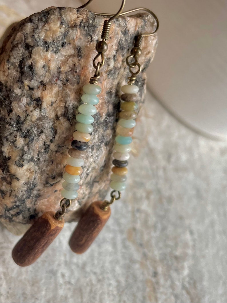 Peut inclure: Boucles d'oreilles faites &agrave; la main avec une cascade de petites perles color&eacute;es dans les tons de bleu, beige et marron. Les perles sont enfil&eacute;es sur un fil et fix&eacute;es &agrave; un charm en bois cylindrique. Les boucles ont un crochet en laiton vintage.