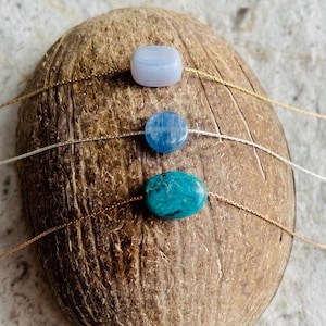 May include: Three necklaces with different colored stones on a brown coconut shell background. The top necklace has a light blue stone, the middle necklace has a blue stone, and the bottom necklace has a turquoise stone.