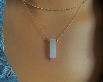 May include: A delicate gold chain necklace with a clear, frosted crystal pendant in the shape of a long, pointed rectangle.