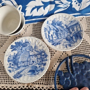K&ouml;nnte beinhalten: Zwei blaue und wei&szlig;e Keramikteller mit einem Cottage-Motiv. Die Teller liegen auf einer wei&szlig;en H&auml;keldeckchen.