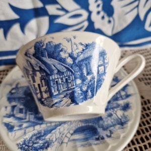 K&ouml;nnte beinhalten: Ein blaues und wei&szlig;es Tee-Set mit einem Cottage-Motiv. Die Tasse hat einen Henkel und die Untertasse einen gewellten Rand.