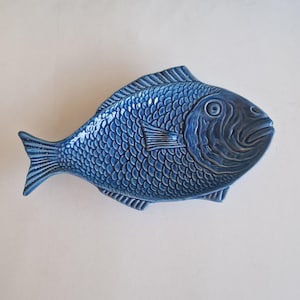 Peut inclure: Un plat de service en céramique en forme de poisson, de couleur bleu foncé. Le plat présente des écailles, des nageoires et un œil proéminent détaillés, créant une apparence réaliste. Le plat en forme de poisson est un objet décoratif et fonctionnel.