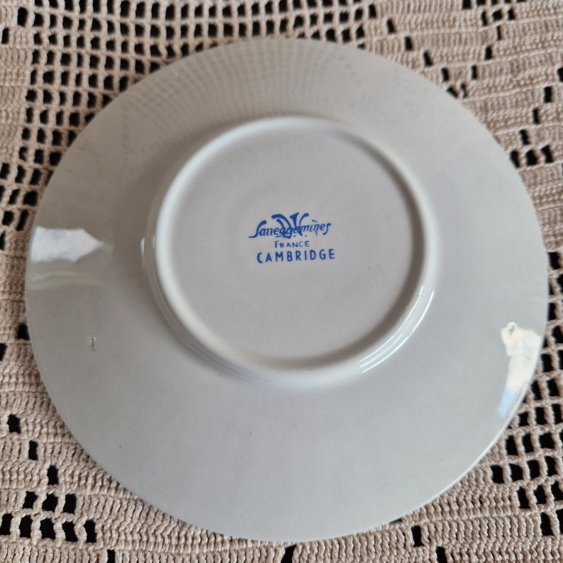 K&ouml;nnte beinhalten: Wei&szlig;e Keramik-Untertasse mit einem blau-wei&szlig;en Logo, auf dem "Sarreguemines France Cambridge" steht.