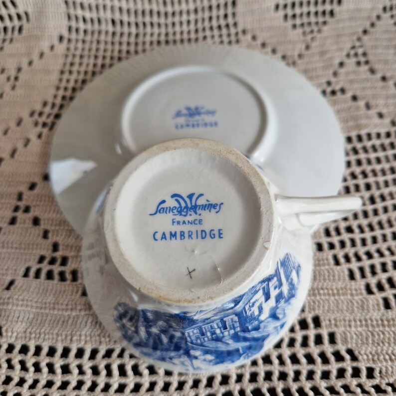 K&ouml;nnte beinhalten: Eine wei&szlig;e Teetasse und Untertasse mit einem blauen und wei&szlig;en Blumenmuster. Der Boden der Teetasse tr&auml;gt den Text "Sarreguemines France Cambridge" in Blau.