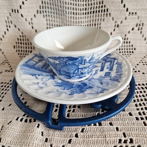 K&ouml;nnte beinhalten: Eine wei&szlig;e Teetasse und Untertasse mit einem blauen und wei&szlig;en Blumenmuster. Die Teetasse hat einen Henkel und die Untertasse einen gewellten Rand. Die Teetasse und Untertasse stehen auf einem blauen und wei&szlig;en Untersetzer.