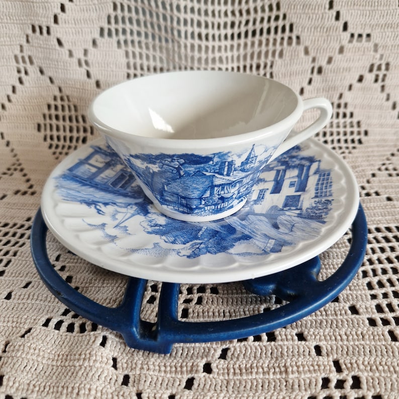 K&ouml;nnte beinhalten: Eine wei&szlig;e Teetasse und Untertasse mit einem blauen und wei&szlig;en Blumenmuster. Die Teetasse hat einen Henkel und die Untertasse einen gewellten Rand. Die Teetasse und Untertasse stehen auf einem blauen und wei&szlig;en Untersetzer.