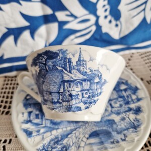 K&ouml;nnte beinhalten: Eine wei&szlig;e Teetasse und Untertasse mit einem blauen und wei&szlig;en Blumenmuster. Das Muster zeigt ein H&auml;uschen mit einer Kirche im Hintergrund.