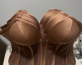 May include: A brown corset with a sweetheart neckline. The bodice is made of a satin-like material, and the lower portion features sheer panels with vertical boning. The corset is displayed on a white surface.