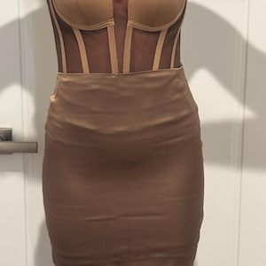 May include: A tan mini dress with a strapless corset bodice and a fitted skirt. The bodice has sheer panels and vertical boning. The skirt is a smooth, fitted mini skirt. The dress is made of a satin-like material.