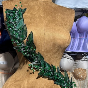 May include: A brown fabric mannequin with a green leaf and bead embellishment on the bodice.