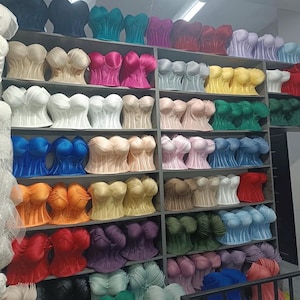 May include: A collection of strapless corset tops displayed on shelves in a wide variety of solid colors including blue, pink, yellow, green, red, orange, white, and beige. Each top features a structured bodice with molded cups and vertical seams.