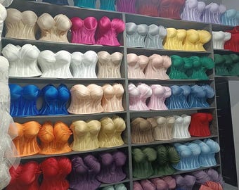 May include: A collection of strapless corset tops displayed on shelves in a wide variety of solid colors including blue, pink, yellow, green, red, orange, white, and beige. Each top features a structured bodice with molded cups and vertical seams.